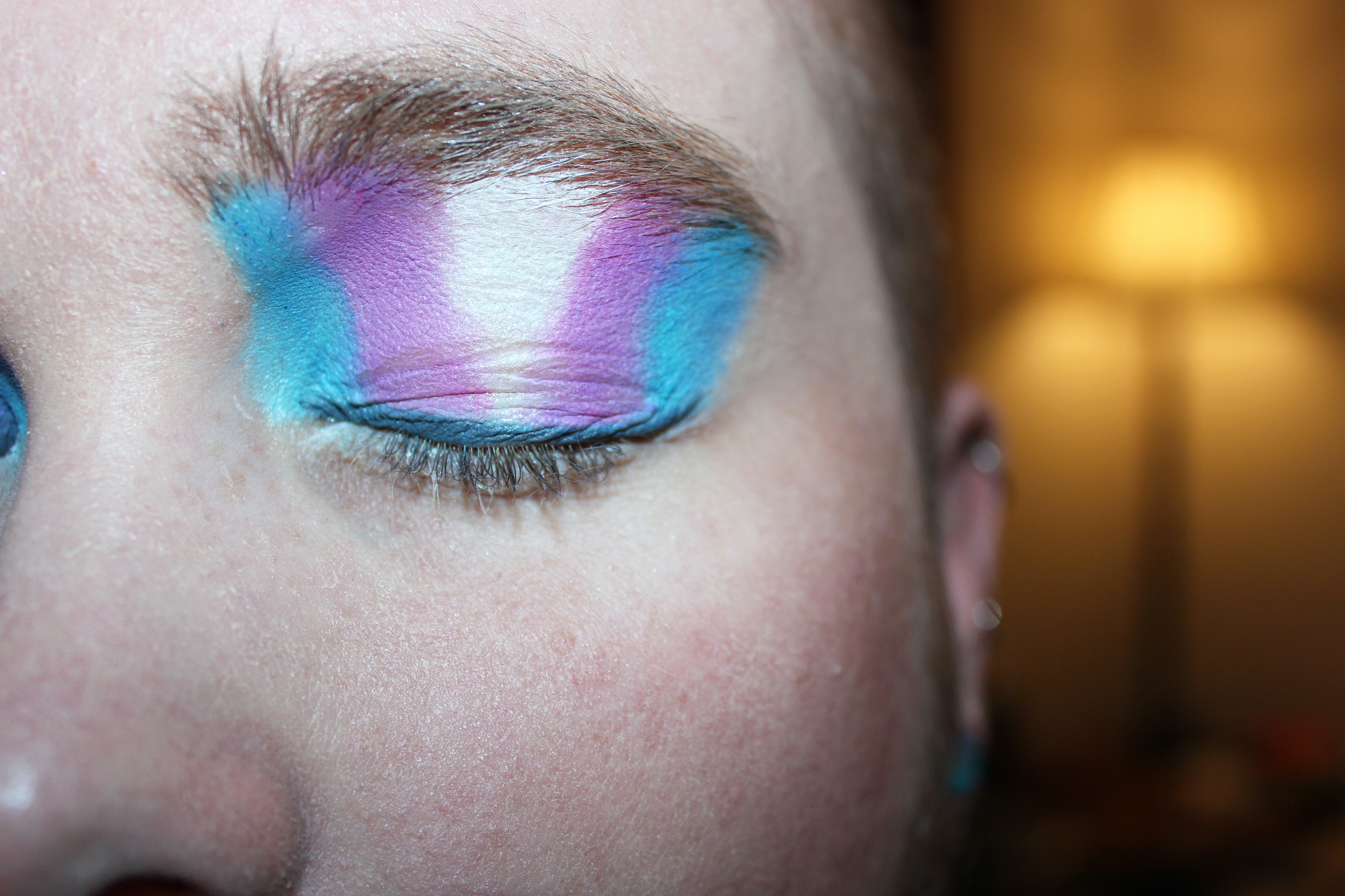 Un gros plan de l'œil d'une personne. Le maquillage est aux couleurs du drapeau de la fierté transgenre.