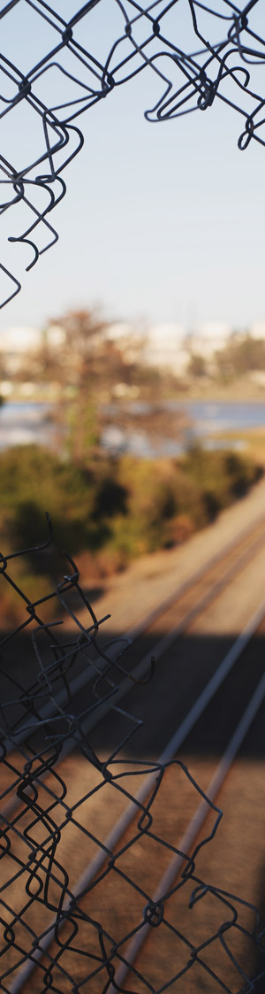 Two railroad tracks seen through a hole in a chain-link fence