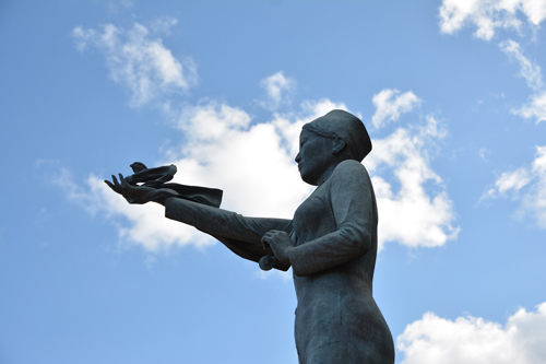 A statue of a woman with her arm outstretched. A dove rests upon her hand.