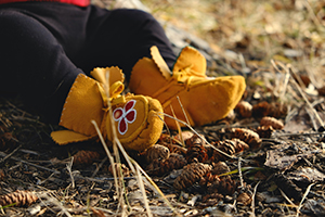 Closeup of a child’s feet in the grass wearing traditional moccasins.