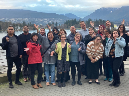 A group of people pose playfully against a background of mountains and water