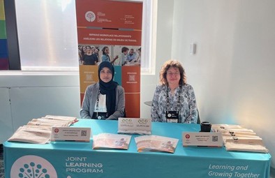 Rini et Karen sont assises derrière une table remplie d’informations et d’articles promotionnels du PAM