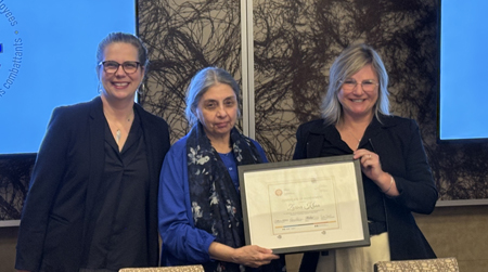 Zarina stands between Catherine and Roxanne, holding the certificate presented to her