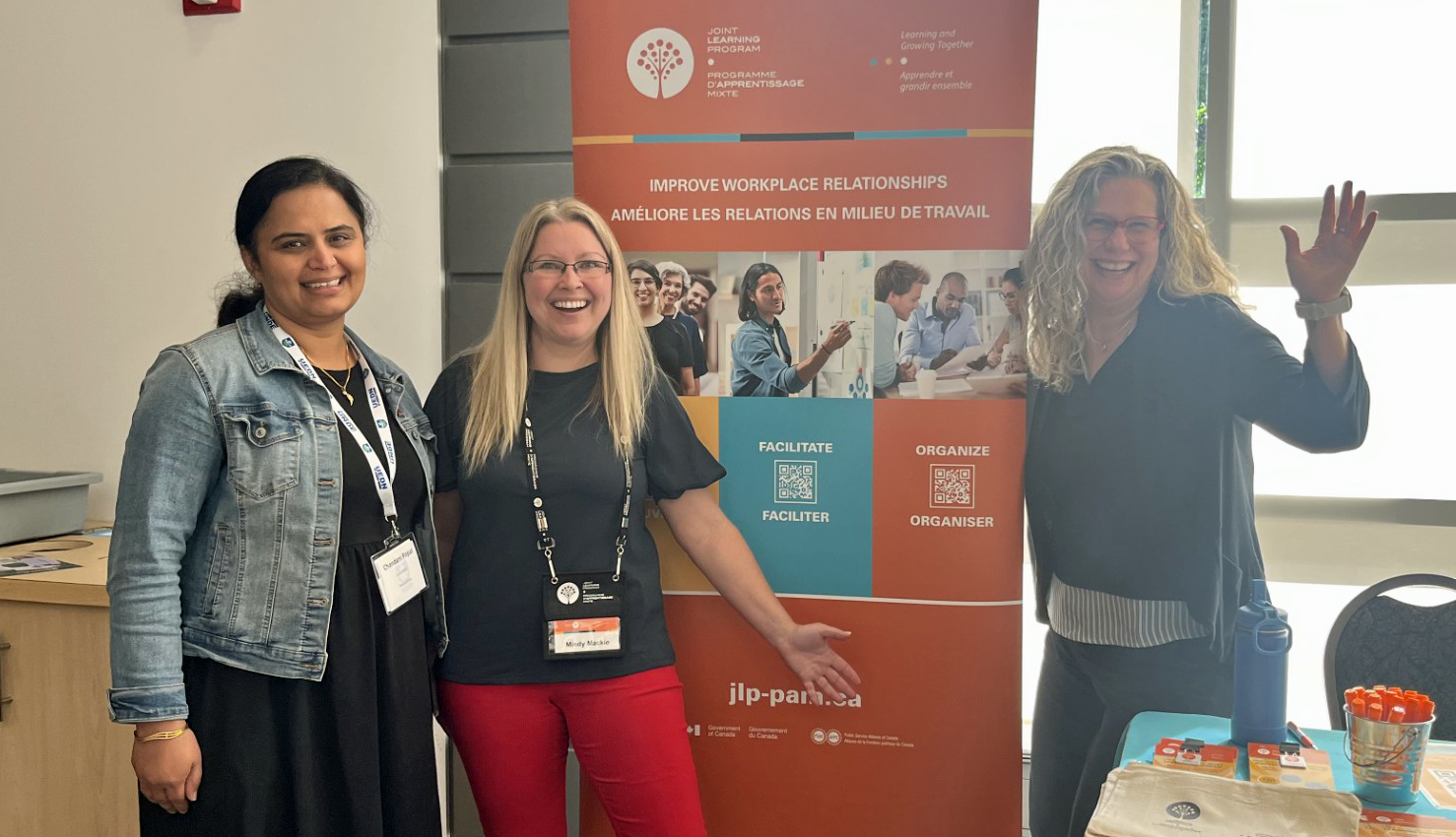 Chandani, Mindy and Roxanne smile and wave in front of the JLP popup banner